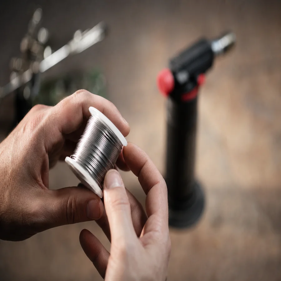 Technician holding silver solder wire spool with torch in background